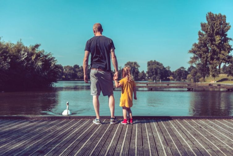 Vader en dochter staan bij een plas kijkend naar een zwaan die komt aanzwemmen
