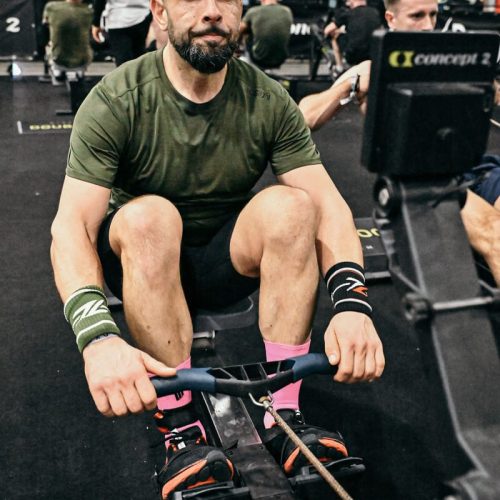 Man with a beard exercising on a Concept2 rowing machine during a fitness event.